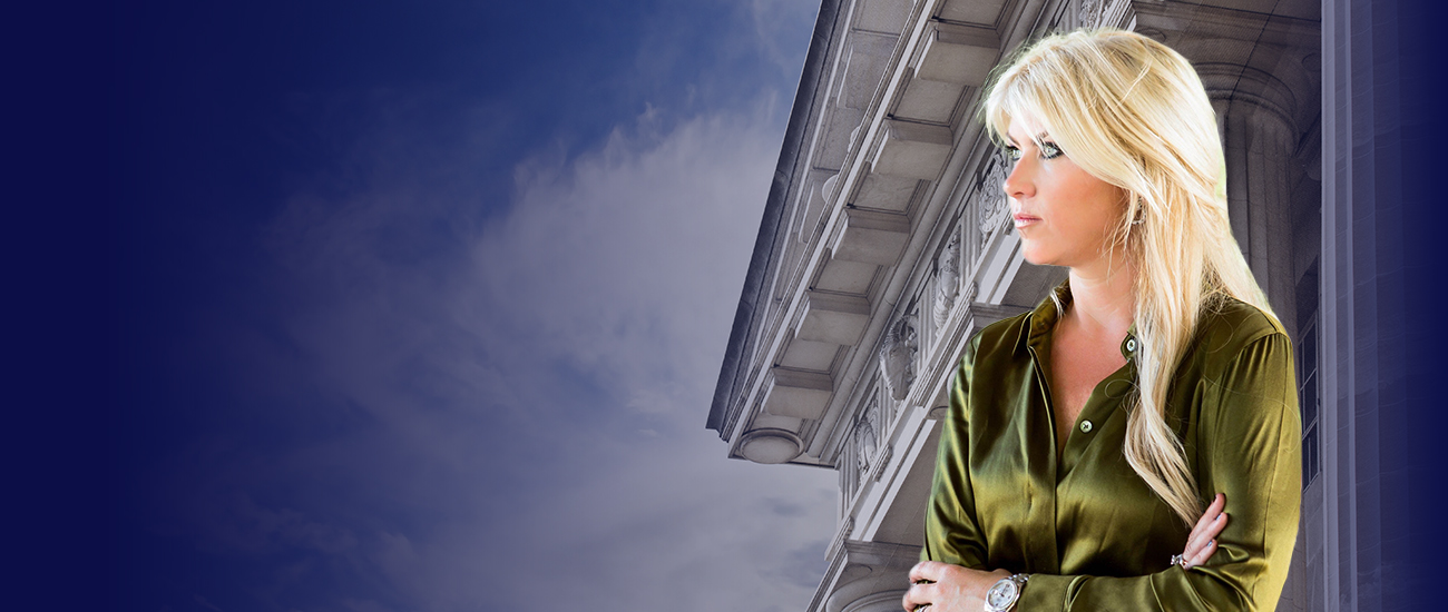 A woman with blonde hair and blue eyes gazes out of a window, lost in thought.